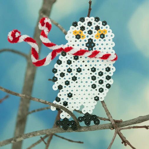 Harfang des neiges blanc et noir en perles à repasser, avec une canne à sucre en fil chenille, posé sur une branche
